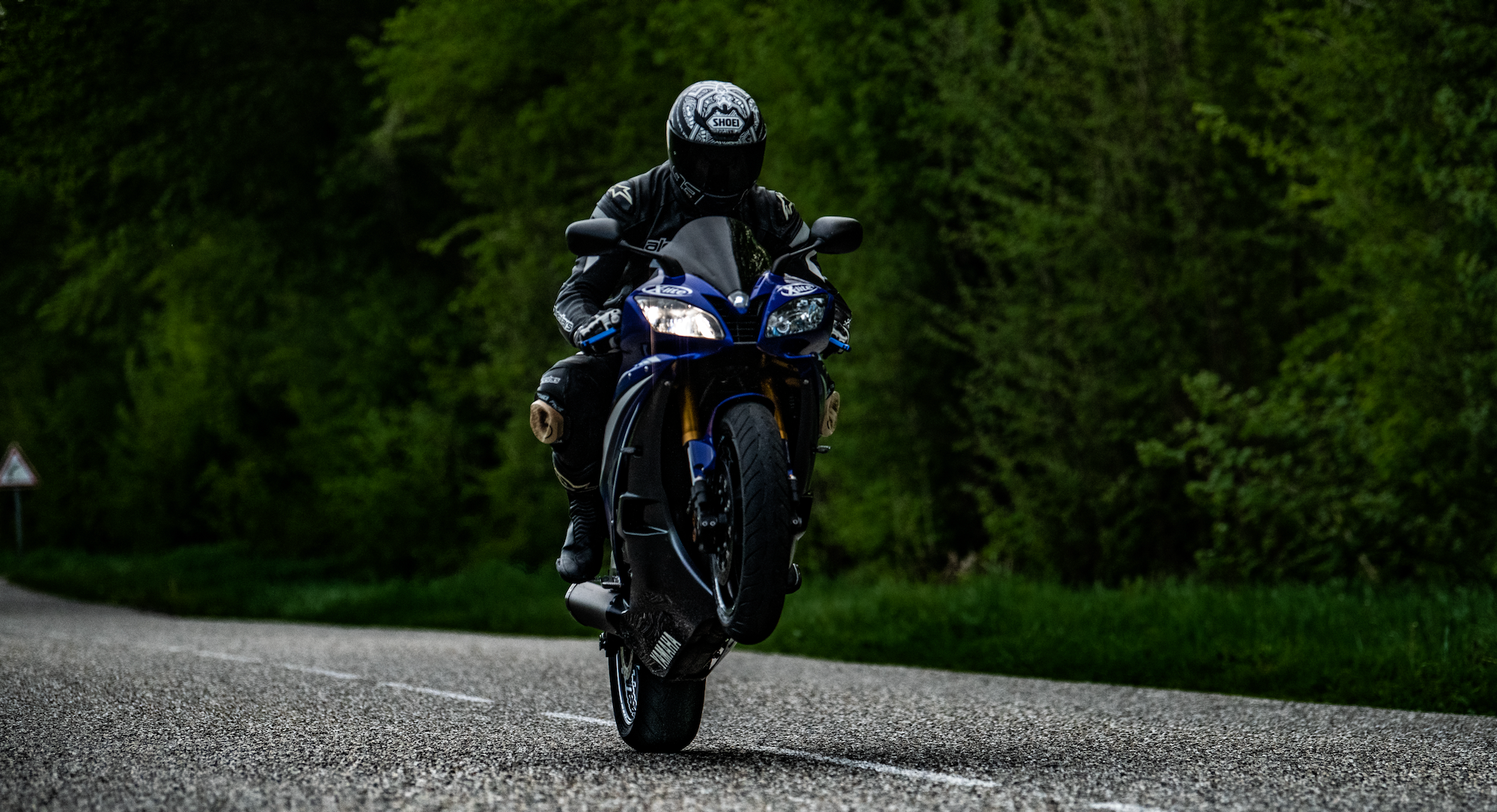 Motorradfahrer mit schwarzer Kleidung auf einer Waldstraße